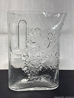 Front view of a clear glass pitcher with textured grapevine motif and integrated handle.