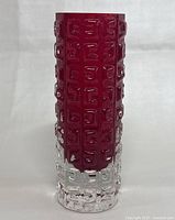 Front view of tall cylindrical glass vase showing Greek key textured pattern in red and clear glass.