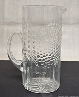 Full side view of clear embossed glass pitcher with Flora pattern and handle
