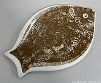 Top side of ceramic fish-shaped plate with brown detailed fish illustration on white background.