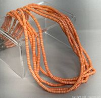 Photo showing the full multi-strand peach coral bead necklace displayed on a clear stand.
