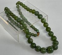 Full view of the 21-inch nephrite green jade bead necklace laid out on a clear stand.