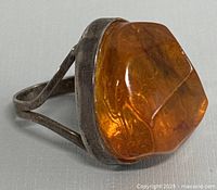 Close-up side view of vintage amber ring showing faceted amber stone within silver setting and split band design.