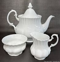 Photo showing the full set of white Royal Albert bone china tea pot, sugar bowl, and creamer with ridged design and curved handles.