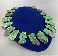 Full view of the necklace displayed on a blue form, showcasing the freeform green jasper slab stones with natural brown veining and green spacer beads.