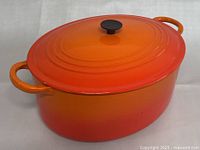 Full front view of orange-red oval dutch oven with lid closed