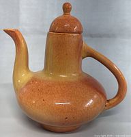 Front angle of the vintage ceramic coffee/tea pot showing the bulbous body, tall neck, curved spout, and handle with a warm orange glaze.