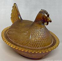 Front angled view of amber glass hen on nest lidded bowl showing detailed feathers and bead rim.