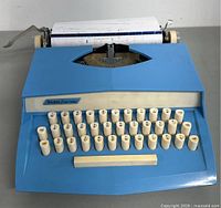 Front/top angled view of blue Sears Easy Touch typewriter with cream keys, showing keyboard and paper loaded into platen roller.