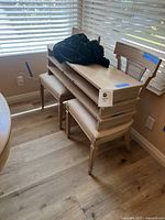 Two wooden chairs with cane backrests, stacked with three table leaves and a dark green fitted tablecloth on top, situated near a window with blinds.