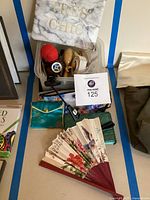 Lot contents showing sewing kit supplies, makeup bags, jewelry bags, book lamp clip, keychains, and decorative fan.