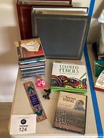 Photo showing two large leather-bound photo albums, a box of colored pencils, a stack of CDs, a pink cat clip, a vintage staple remover, a Jewish-themed DVD, and a decorative bookmark.