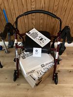 Front view of rollator with black padded seat and maroon frame, with sealed Ultrasorbs pads box underneath