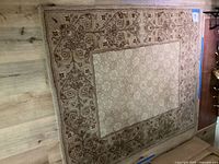 Full view of the brown and beige rectangular area rug laid on a wood floor, showing its ornate floral pattern and bordered design.
