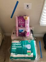 Used adult diapers in unopened packages, including Poise pads and Walgreens Certainty Stretch Briefs, stacked along with absorbing bed pads.