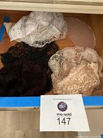 Photo showing six lace head coverings in white, ivory, black, and darker shades inside a drawer.
