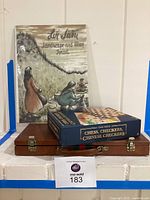 Photo of stacked items including Chess, Checkers, Chinese Checkers boxed set, wooden Rumikub case and three lithographs by Zvi Livni titled Landscape and Man Israel leaning behind