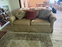 Front view of the brown fabric sleeper sofa with three throw pillows and carpet underneath.