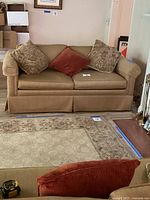 Full front view of the brown fabric pull out couch with three decorative throw pillows in beige pattern and rust color.