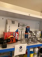 Shelf with boxed Frigidaire water filters, red box of ACME tape, assorted light bulbs, and Black & Decker power screwdriver with charger