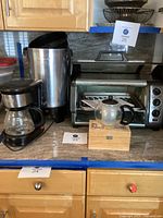 Countertop photo showing Hamilton Beach toaster, Living Solutions coffee maker, West Bend percolator, tea pot on wooden box, and a toaster oven in background