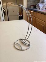 Silver metal banana hanger on kitchen counter with curved hooks and round base.
