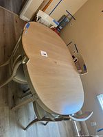 Oval light wood dining table with four chairs surrounding it, view from a corner showing shape and overall size.