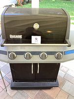 Front view of the Ducane barbecue grill showing four control knobs and black hood with logo.