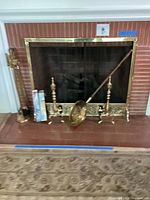 Full view of the brass fireplace screen with tools and long matches set in front of fireplace.