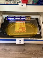 Photo of black hot plate, yellow plastic serving tray, roll of Reynolds freezer paper and plastic refrigerator shelf liners inside a drawer