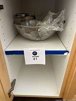 Large etched glass hibiscus punch bowl wrapped in plastic on a shelf.