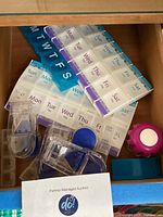 Photo of several weekly pill organizers with day and AM/PM compartments and multiple plastic pill cutters in drawer.