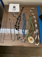 Photo showing the collection of various necklaces with beads, faux pearls, pendants, a wristwatch, and earrings arranged on a wooden surface.
