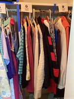 Photo of sweaters and long sleeve tops on hangers in closet rack showing range of colors and patterns, mostly winter and casual wear.