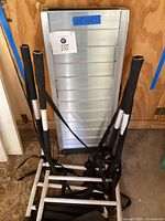 Photo of metal wheelchair ramp with attached size label 28x36 and wheelchair rack with foam-padded handles and securing straps in front.