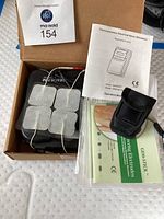 Photo showing nerve stimulator device, electrode pads, pulse monitor pouch, and operation manual inside cardboard box.