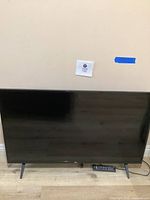 Front view of LG 43 inch flat screen TV with remote placed on floor in front of TV.