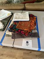 Multiple sets of placemats with varied colors and patterns stacked on a table, including plain and colorful fabric mats plus cloth napkins.