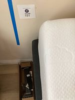 Partial view of mattress and box with bed parts on floor beside it.