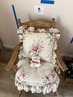 Front view of wooden rocking chair with floral printed seat and back cushions and small white teddy bear on the seat.