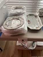 Stack of dishes including dinner plates wrapped partially in bubble wrap and a large hexagonal serving tray on the table.
