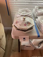 Hexagonal serving bowl with lid and some plates stacked on a table near window blinds.