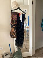 Five scarves of varied patterns and fabrics hanging on a door, showing color and style diversity