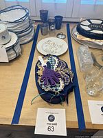 Photo showing various Judaica items on table including decorative box/art piece, kiddush cups, plates, challah cover, and glassware