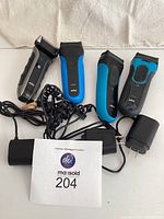 Four Braun handheld shavers in mostly black and blue colors, with three black power cords laid in front of the shavers on a white surface.