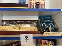 Photo shows the Arthur Court silver plated serving tray with grapevine design, Chef J.P. Maurice carving set in box, and Corning Ware saucepan cradle in original box on blue shelf.