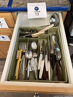 Full drawer view showing assortment of forks, spoons, knives, and other utensils in a plastic compartment organizer.