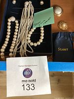 Photo of all jewelry laid out showing pearl necklaces, bracelet, earrings, two brooches, and Stauer pouch in box.