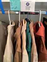 View of six men's coats on hangers showing various colors and materials including white, tan, teal, beige, brown, and rust red coats.