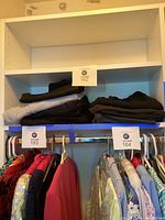 Photo showing five folded sweatpants on a white shelf, four black and one grey, tagged with auction label.